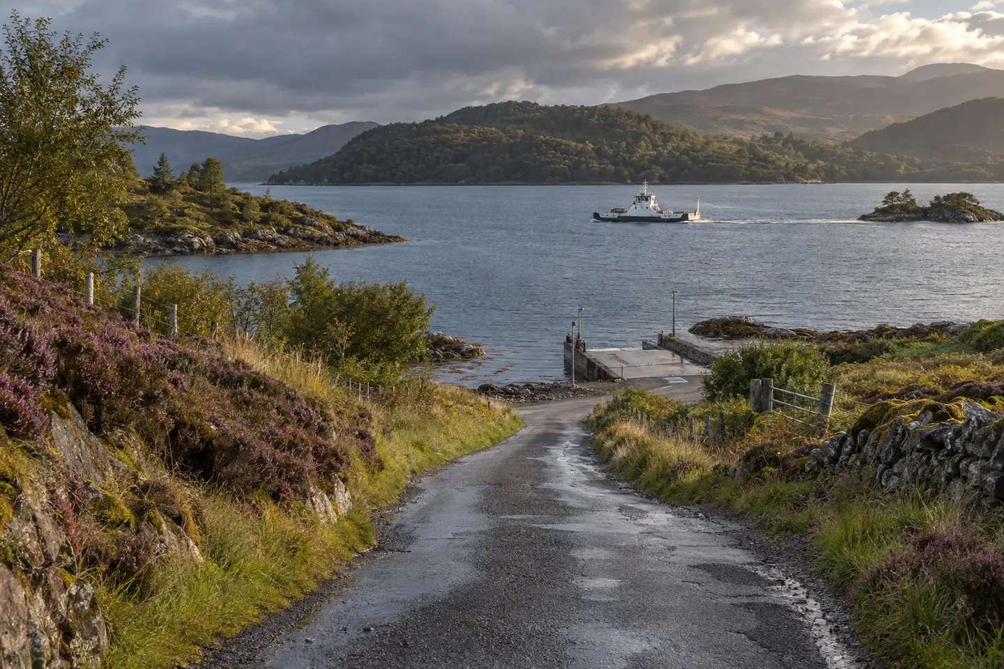 A rain-darkened single-track road descending to a small ferry slip in Argyll